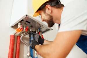 Closeup of plumber using screwdriver while fixing boiler or water heater, working on heating system in apartment. Manual work, maintenance, repair service concept